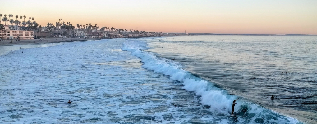 Beach in the city of Oceanside with surfers in the waves at sundown.