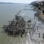 Aerial view of pilings in the water with train tracks to the right of the waterline.