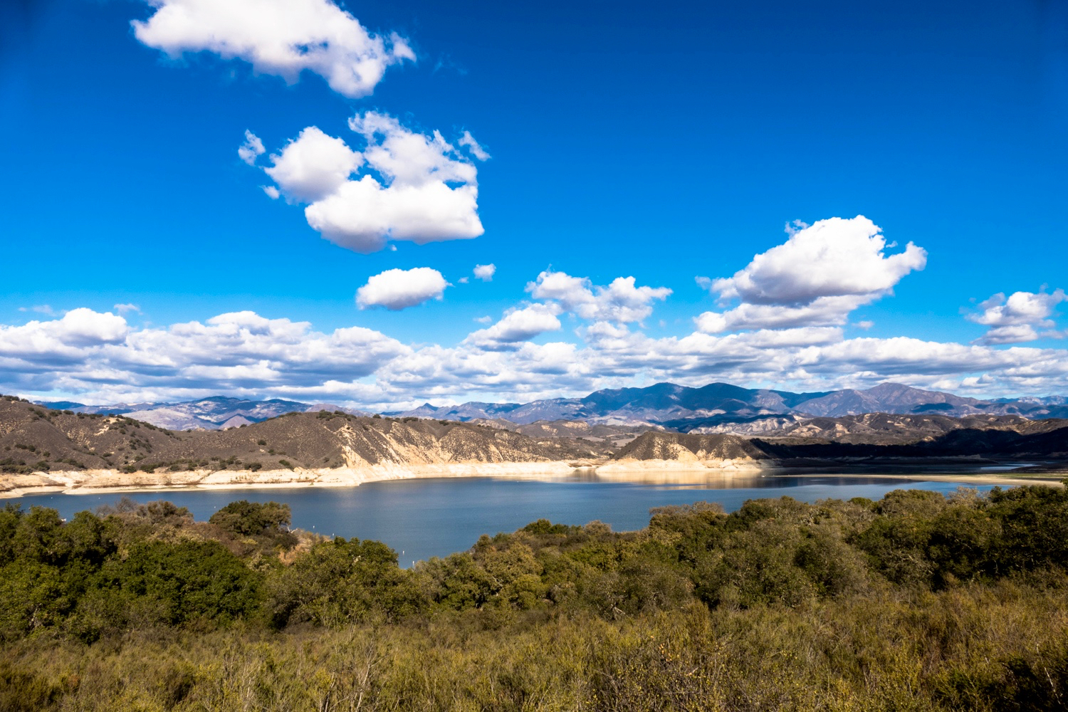 Overlooking the water with mountains in the background and fluffy white clouds against a blue sky in Santa Barbara County. 