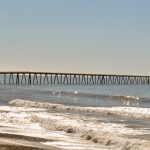 View of the entire Rincon causeway and island, past the beach, small capping waves and a calm sea, from the bike path.