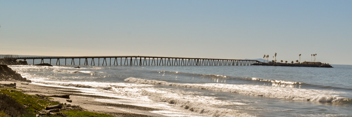 View of the entire Rincon causeway and island, past the beach, small capping waves and a calm sea, from the bike path.