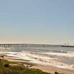 View of the entire Rincon causeway and island, past the beach, small capping waves and a calm sea, from the bike path.
