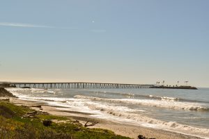 View of the entire Rincon causeway and island, past the beach, small capping waves and a calm sea, from the bike path.