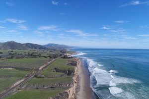 drone image of Hollister Ranch with the empty beaches and green hills to the left and breaking waves and the open Pacific ocean to the right.