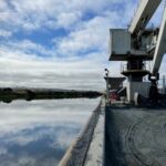 looking past the machinery, down the river, on a sunny day with clouds scattered in the blue sky.