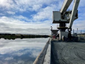 looking past the machinery, down the river, on a sunny day with clouds scattered in the blue sky.
