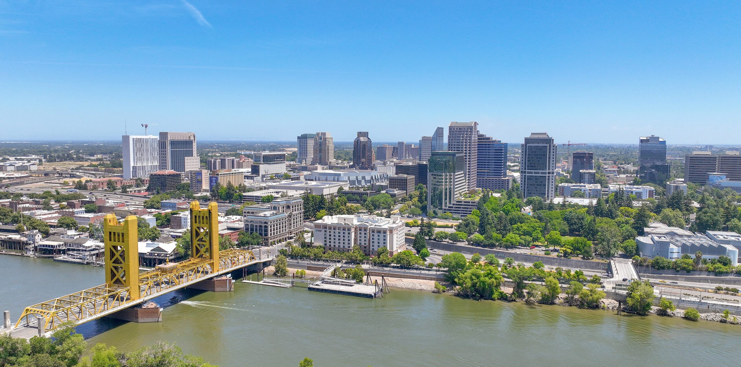 Aerial view of Sacramento on a clear and sunny summer day. The golden Tower Bridge is on the left in the foreground over the Sacramento river, behind is downtown Sacramento.