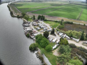 RV Park and camping spaces aerial view of te river to the left and the facilities to the right with agricultural fields in the background.